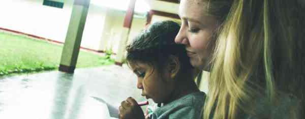 A student looks over a young girl's shoulder as she writes on a piece of paper